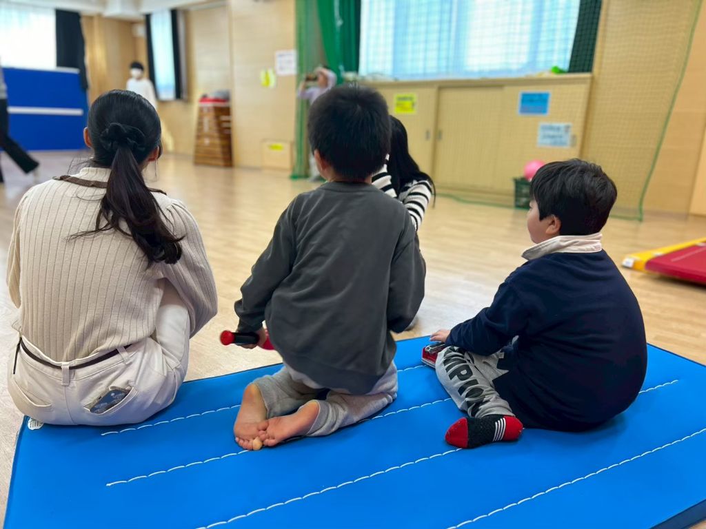 マットに座って学生とこどもが一緒に過ごす様子